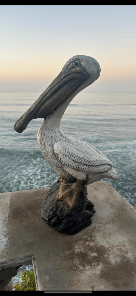A handcrafted cement stone pelican sculpture positioned near the ocean at sunset, showcasing intricate details and a realistic appearance.